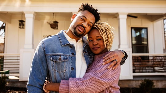 Couple embraces each other standing in front of home